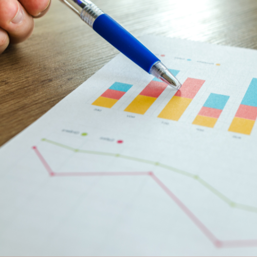 Pessoa apontando para gráfico colorido em papel com caneta azul, representando análise de desempenho ou resultados de crescimento.