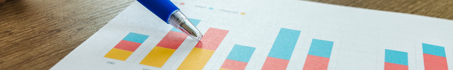 Pessoa apontando para gráfico colorido em papel com caneta azul, representando análise de desempenho ou resultados de crescimento.