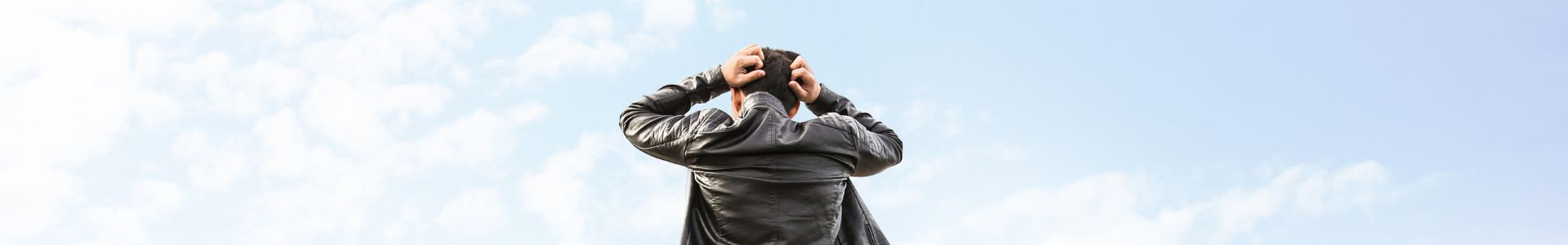 Homem de costas em estrada aberta ajusta o casaco, olhando para o horizonte sob céu claro.