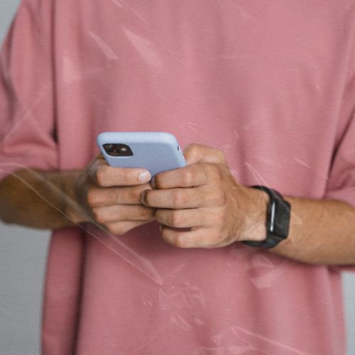 Pessoa segura smartphone com as duas mãos, usando o aparelho em ambiente interno, com relógio no pulso.