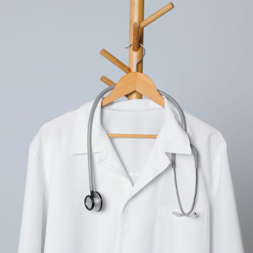 Jaleco médico pendurado em cabide com estetoscópio apoiado, em fundo neutro e ambiente minimalista.